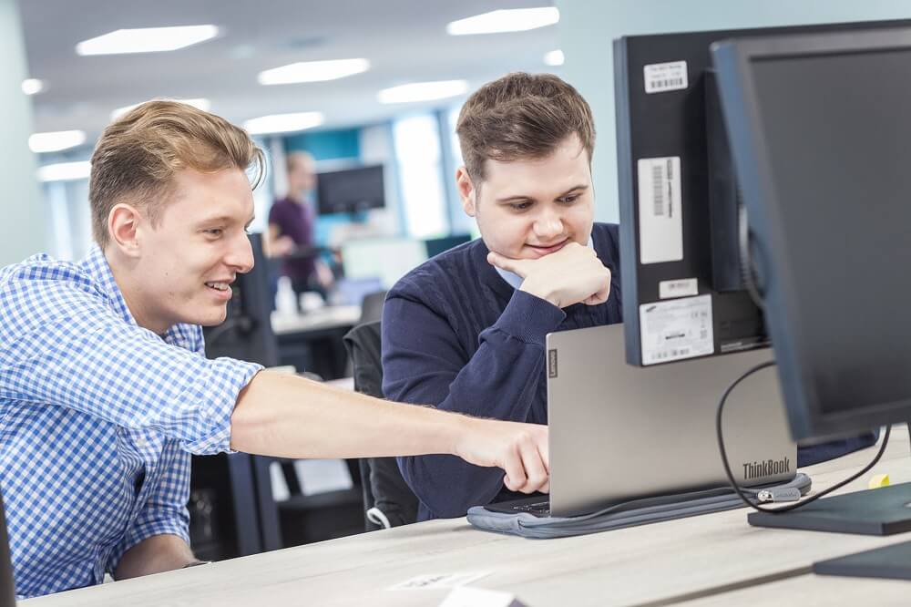 two men in an office discussing work on a laptop
