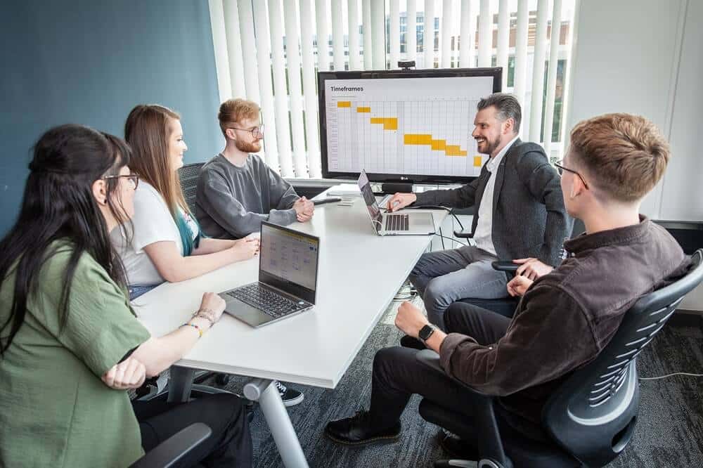 SaaS web design and development team having a team meeting in an office around a desk